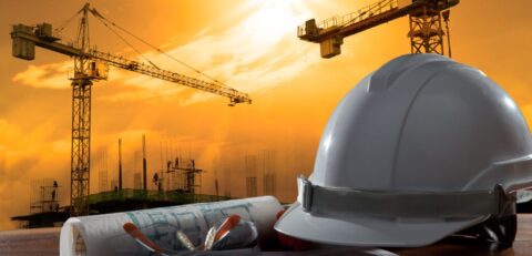 file of safety helmet and architect pland on wood table with sunset scene and building construction